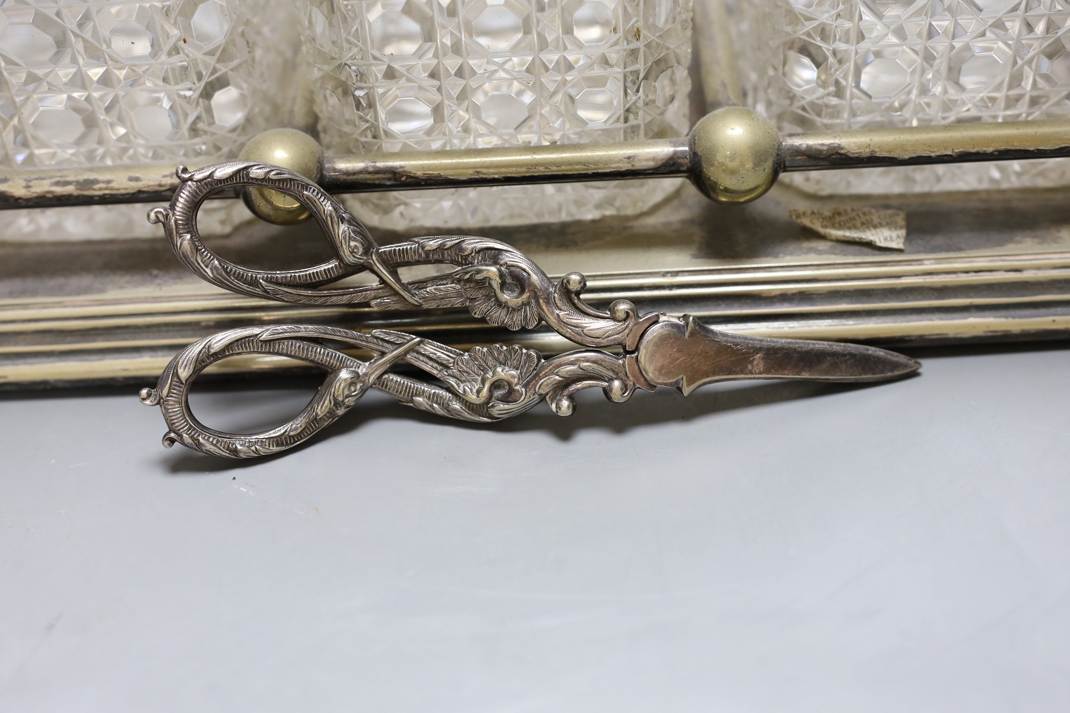 A Victorian electroplate three bottled tantalus, with a silver whisky and gin label plus pair of plated grape scissors, tantalus 33 cms wide